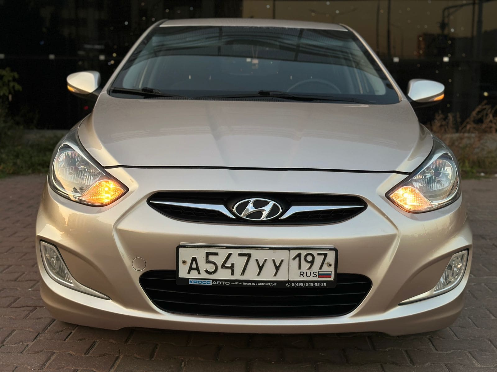Фотография - Передняя часть автомобиля Hyundai светлого цвета с включенными фарами и номерным знаком